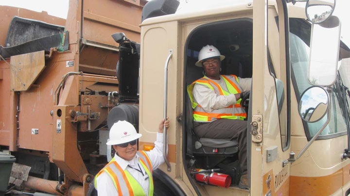 solid waste collection workers getting in a garbage truck